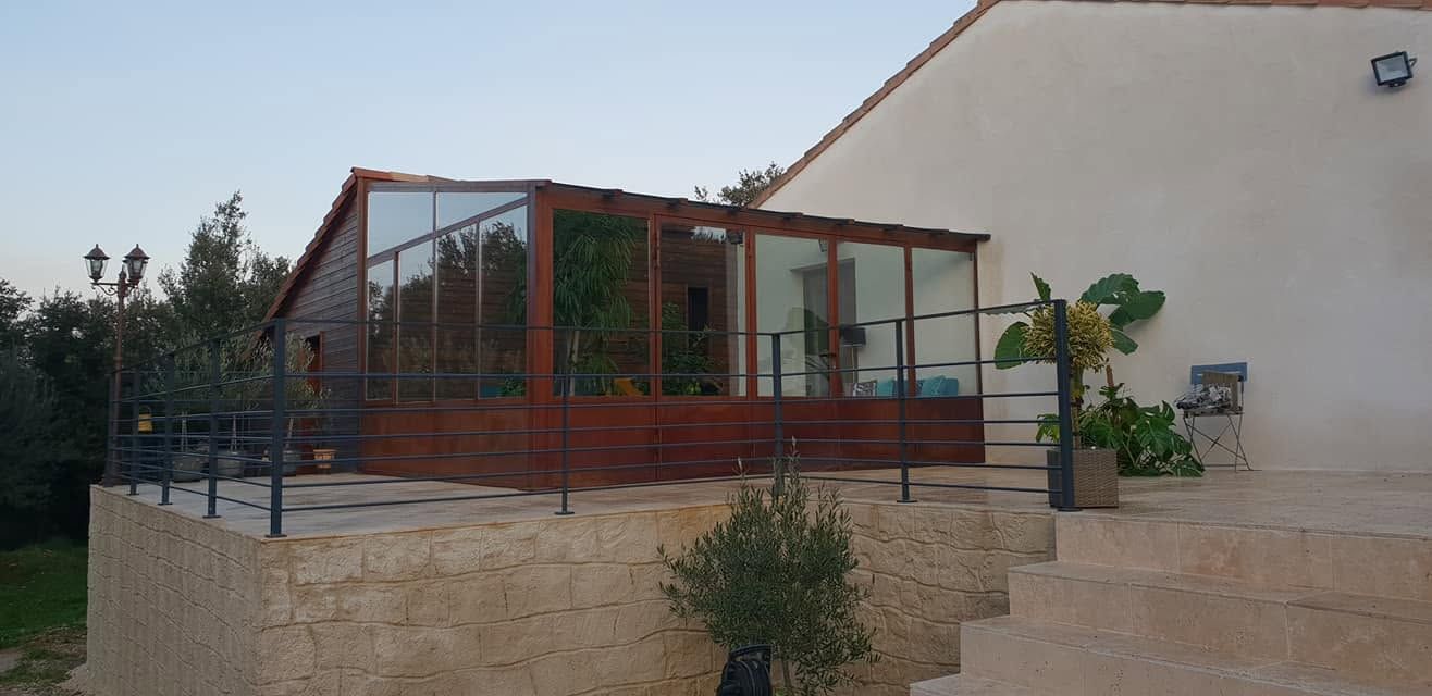 Verrière de salon avec un mur en pierre et escalier dans un jardin ensoleillé.