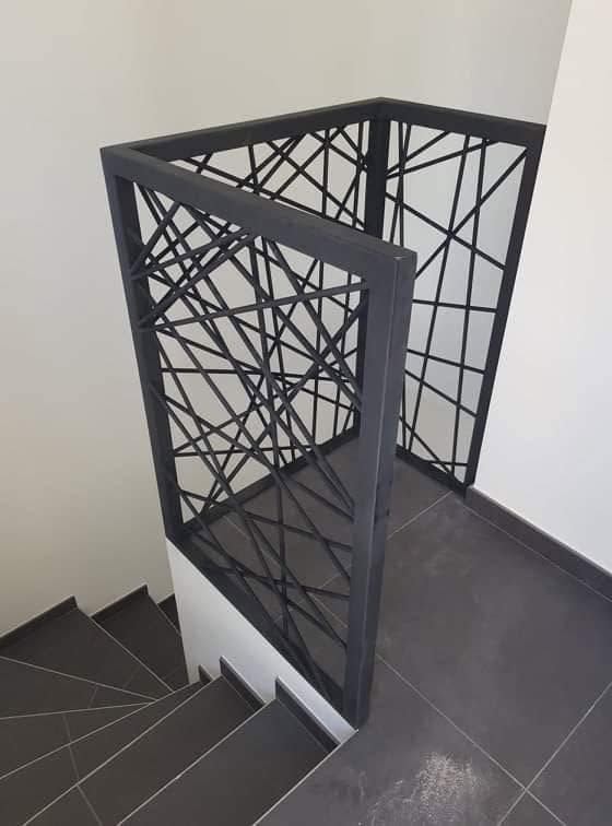 Escalier moderne avec rampes en métal noir et des marches carrelées grises sur un palier.