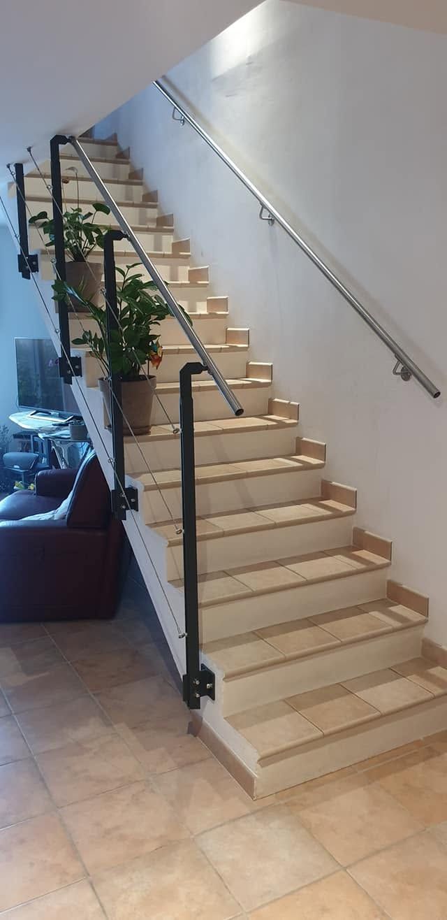 Escalier intérieur avec des marches beiges, et des mains courantes en métal avec des plantes en pot posées sur un sol carrelé.