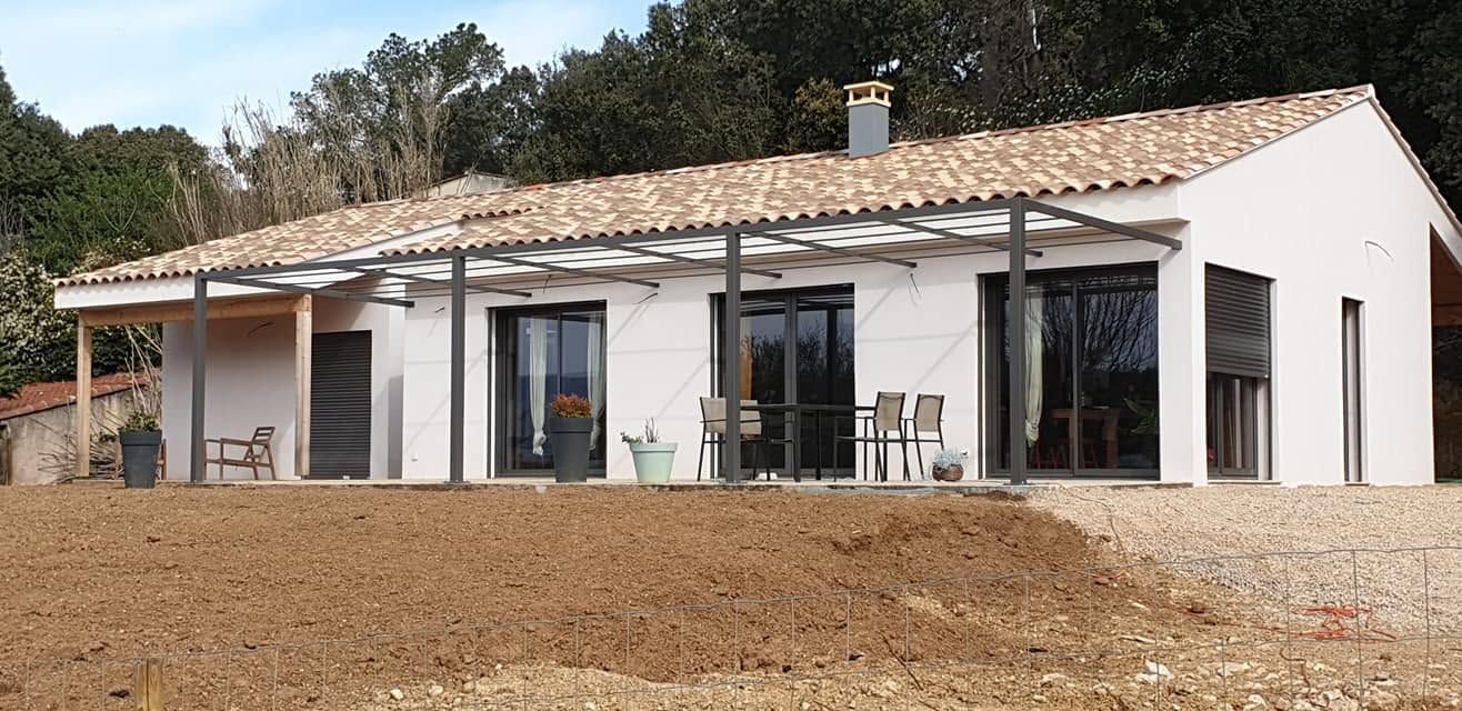 Maison blanche moderne avec un toit de tuiles et de grandes fenêtres sur un terrain en terre.