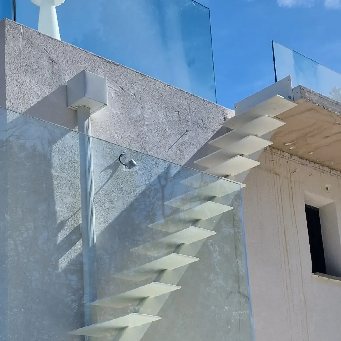 Bâtiment blanc moderne avec une balustrade en verre et un escalier extérieur en zigzag sous un ciel bleu.