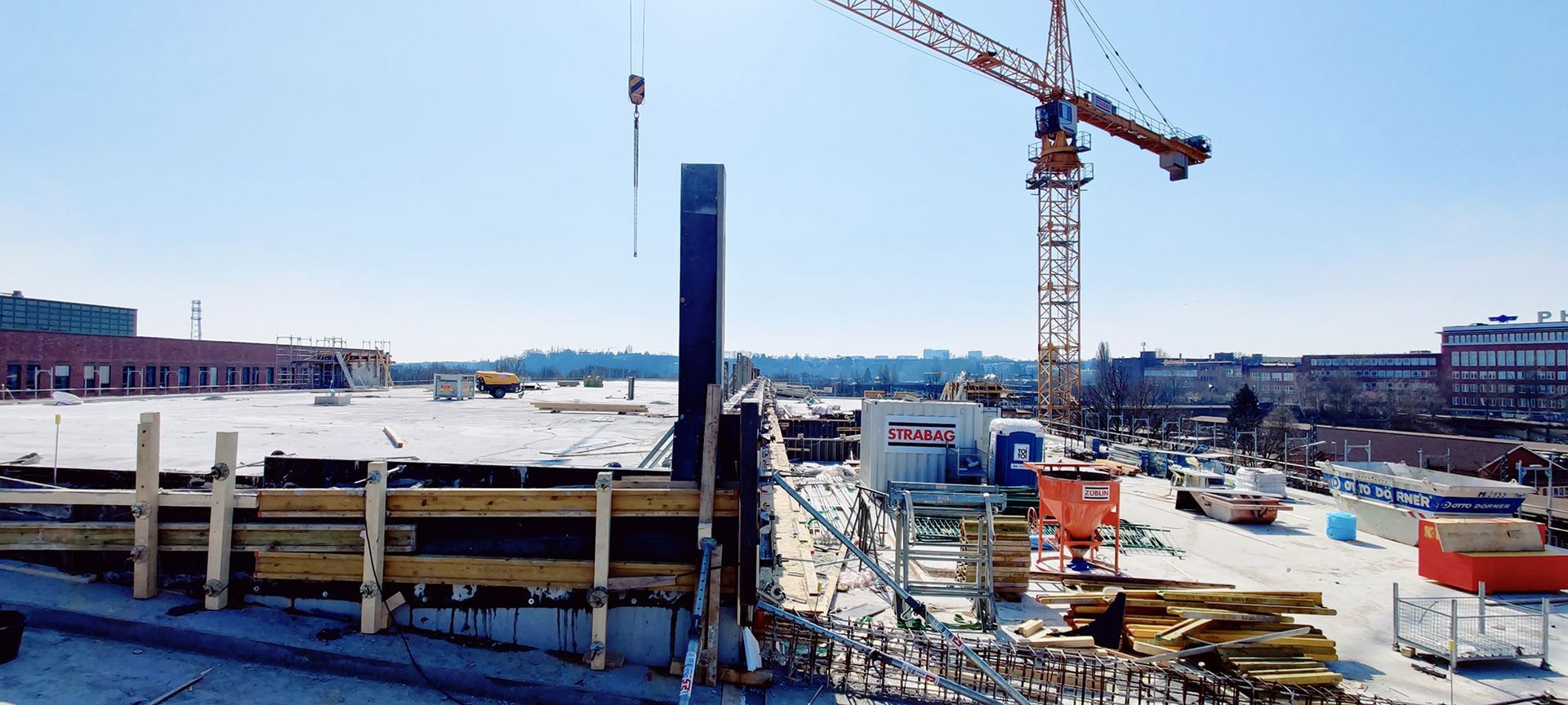 Baustelle mit Kran und teilweise errichteter Betonkonstruktion unter strahlend blauem Himmel