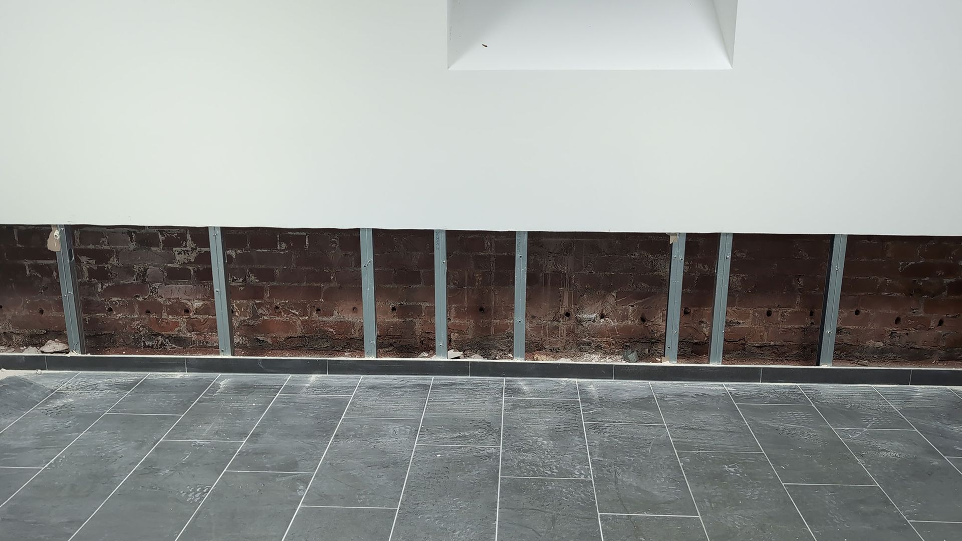 Leerer, gefliester Raum mit weißer Wand, einer Nische und freiliegendem Ziegelstein an der unteren Wand