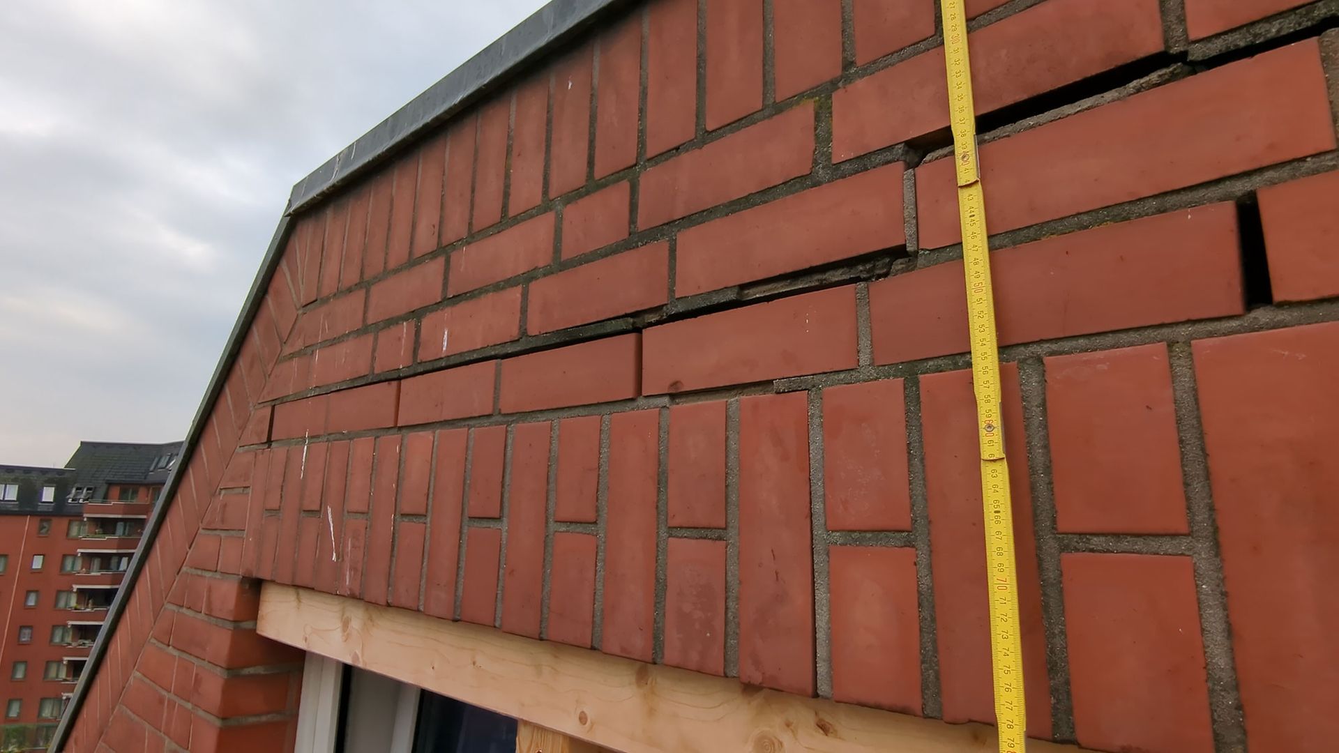 Fassade aus rotem Backstein mit ungleichmäßigem Mauerwerk und sichtbaren Schäden in der Nähe des Dachrandes