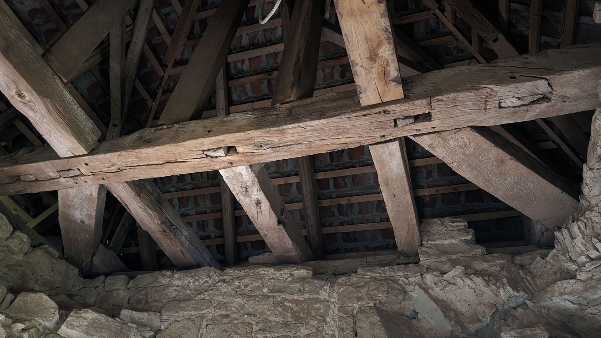 Nahaufnahme von verwitterten Holzbalken und Dachsparren, die eine rustikale Steindecke tragen.