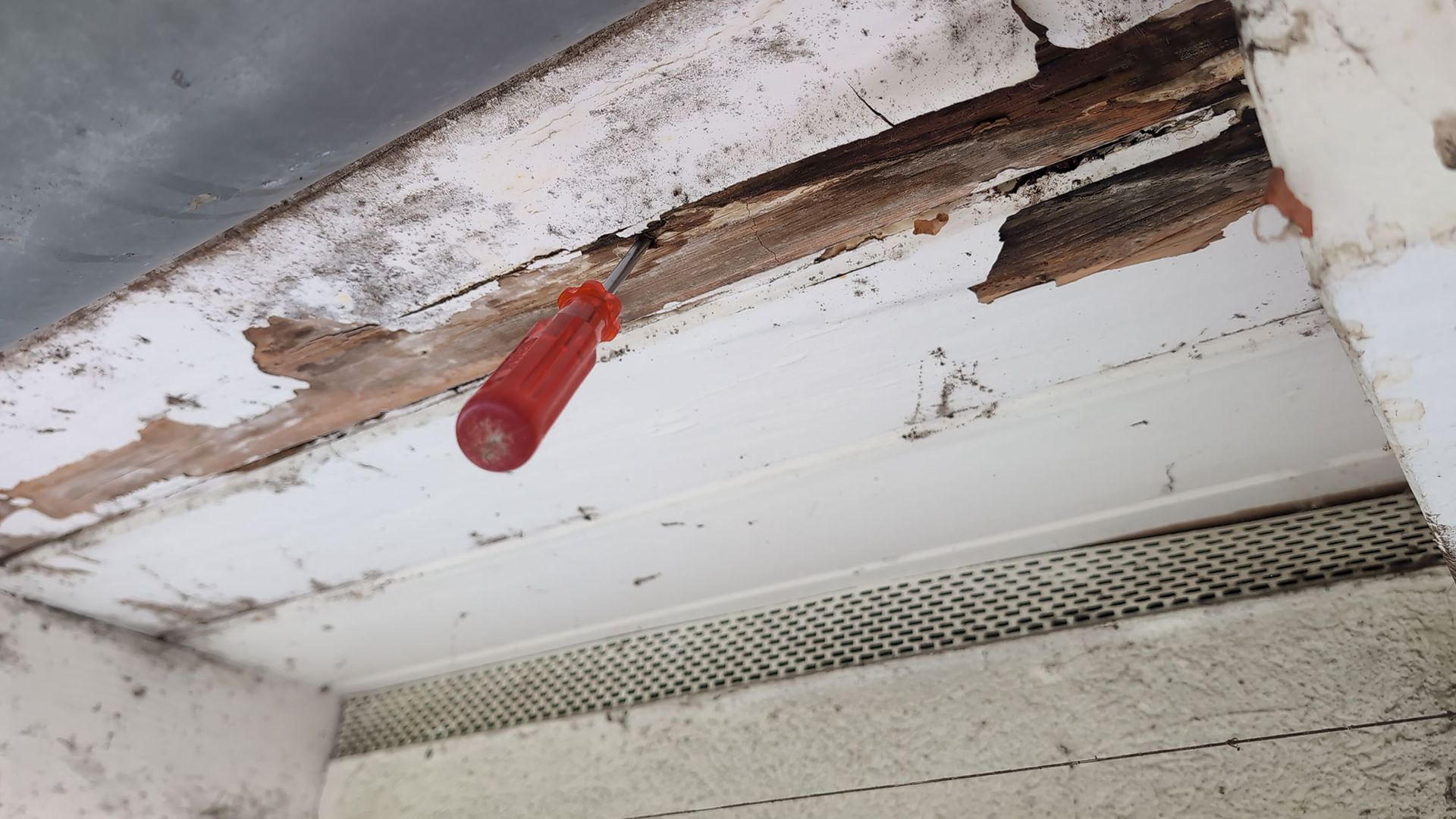 Beschädigte Decke mit abblätternder Farbe, Wasserflecken, freiliegendem Holz und einer herabhängenden roten Lampenfassung