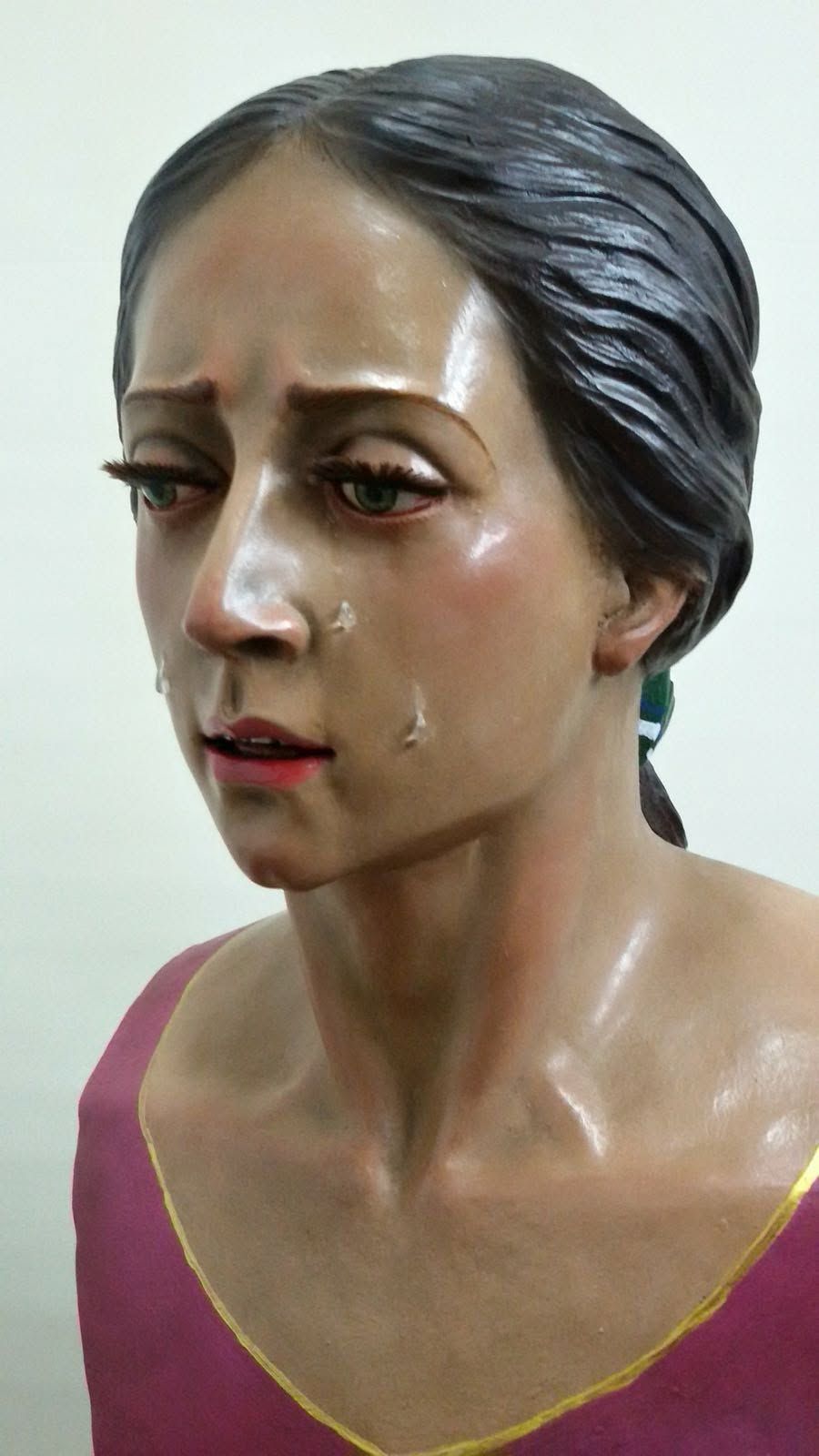 Primer plano de un busto brillante esculpido que representa a una mujer con expresión de dolor, cabello oscuro y ropa rosa.