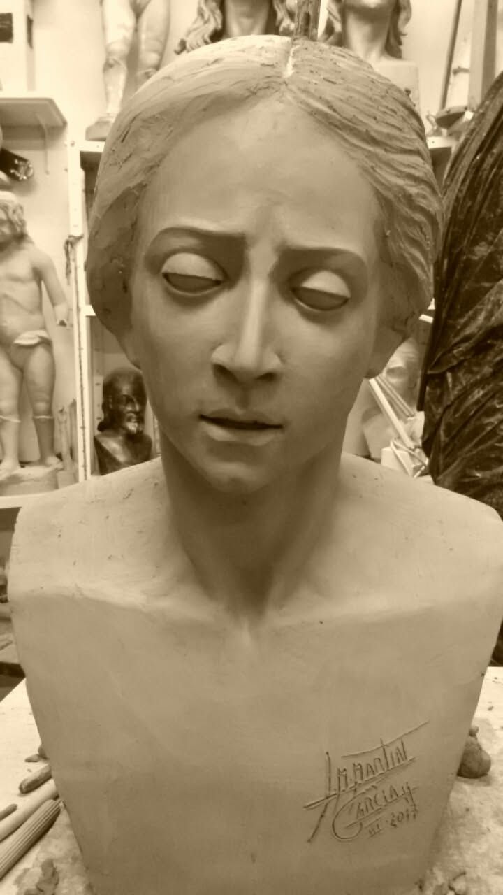 Escultura de busto en tono sepia con los ojos cerrados y expresión neutra, expuesta en una galería interior.
