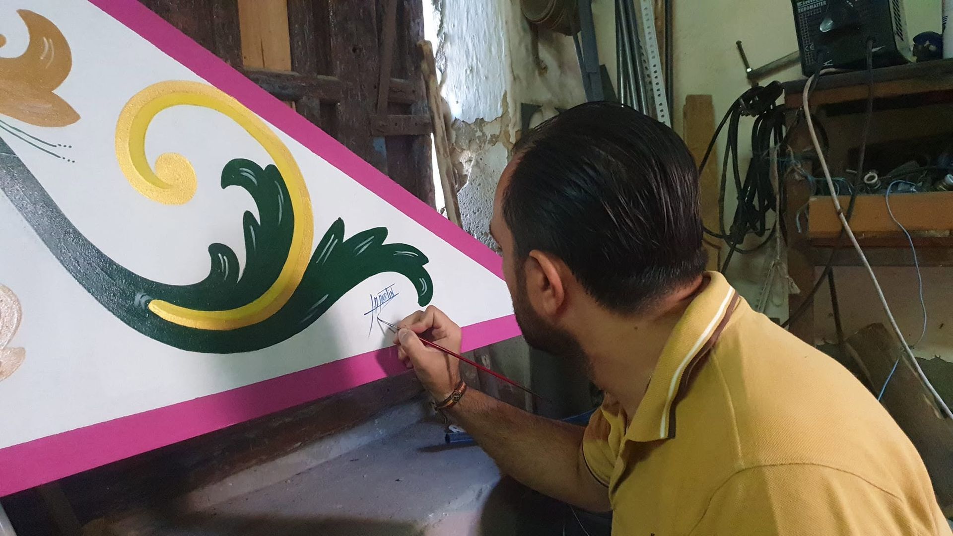 Hombre pintando un remolino decorativo verde y dorado en un panel de pared blanco.