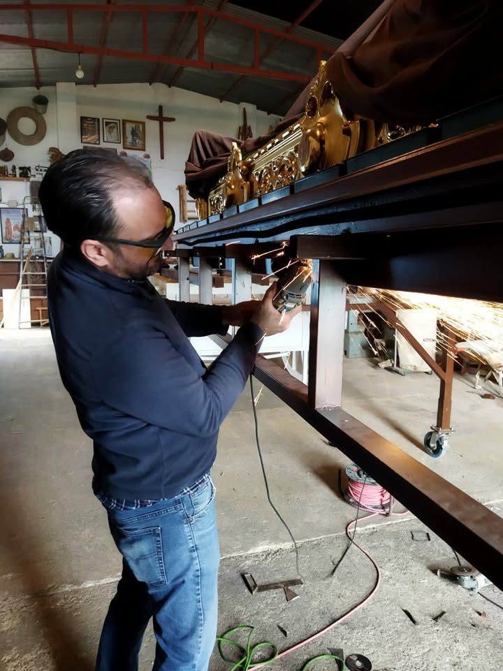 Un hombre inspecciona un objeto grande de color dorado sobre un banco de trabajo en un taller.