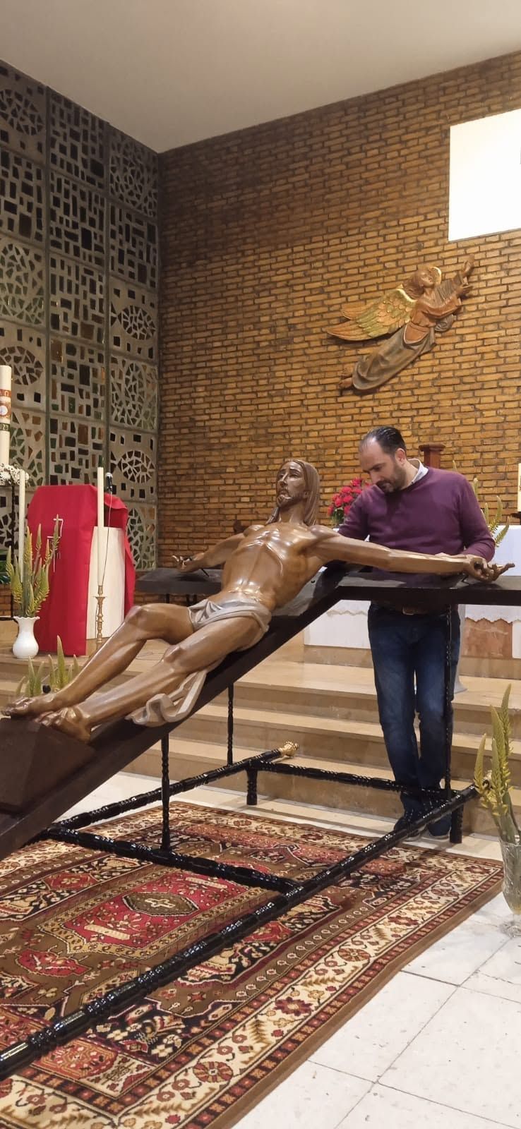 Una persona se inclina sobre una escultura de madera en una habitación decorada con motivos, paredes de ladrillo y alfombras.