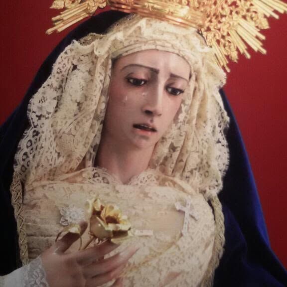 Estatua de un santo con túnica y aureola dorada, sosteniendo un lirio sobre un fondo rojo.