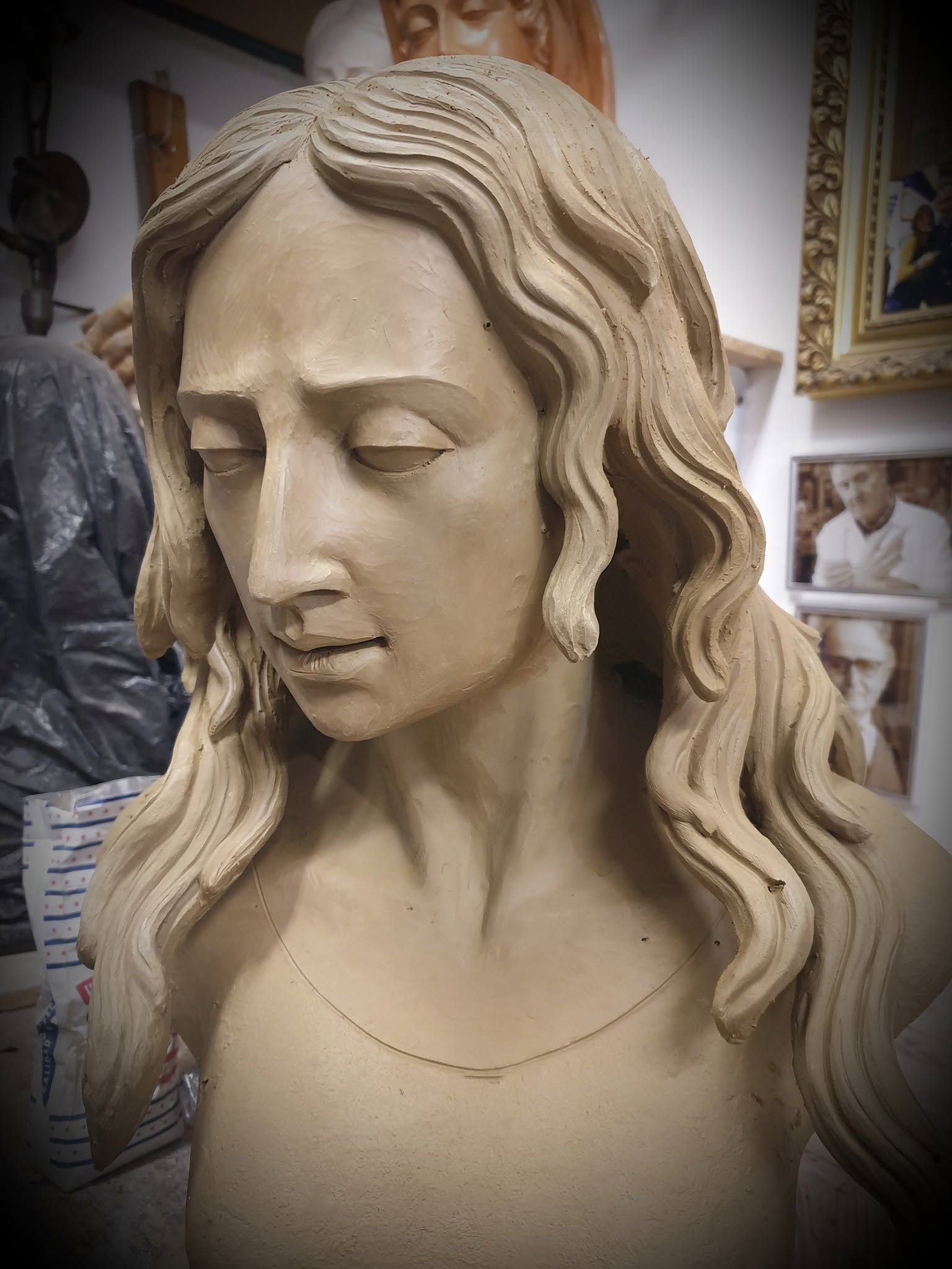 Escultura de busto de arcilla de una mujer con cabello ondulado y expresión solemne en un estudio de arte.