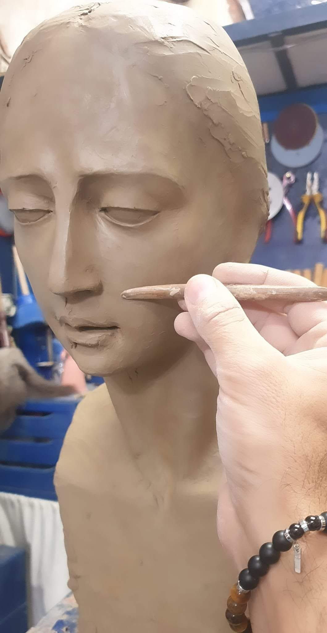 Esculpir a mano la boca y la nariz de un retrato de arcilla con una herramienta pequeña.