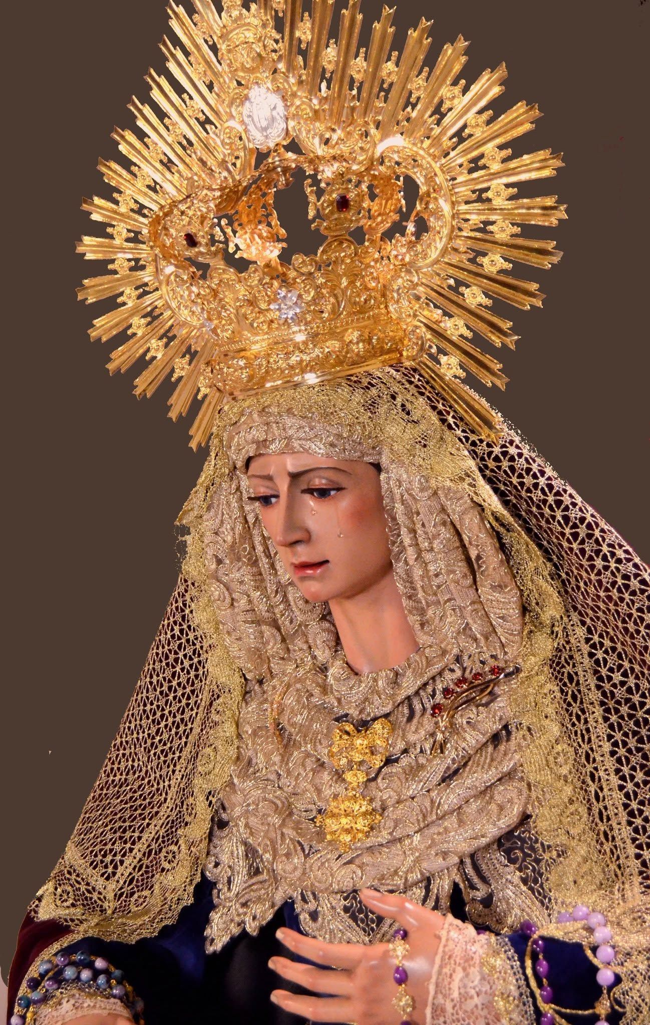 Persona con un elaborado tocado dorado y un velo bordado, mirando hacia abajo, vestida con un atuendo ceremonial decorativo.