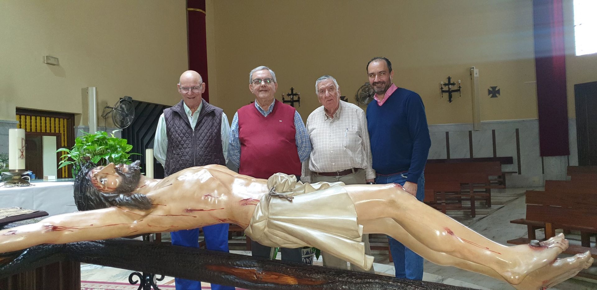 Cuatro hombres se encuentran detrás de una gran estatua de un crucifijo dentro de una iglesia.