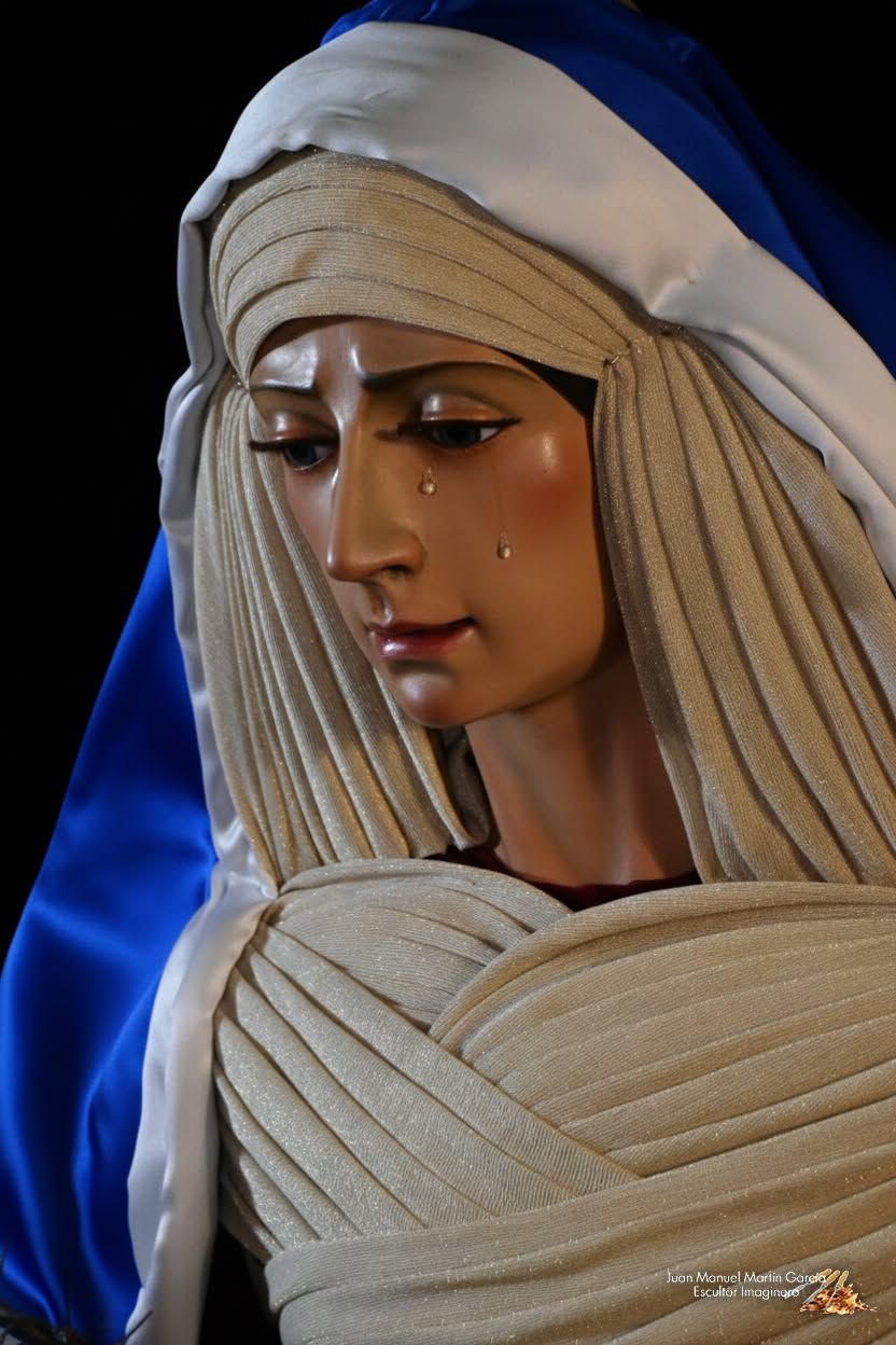 Estatua de una figura velada con túnica color crema sobre un fondo azul oscuro.