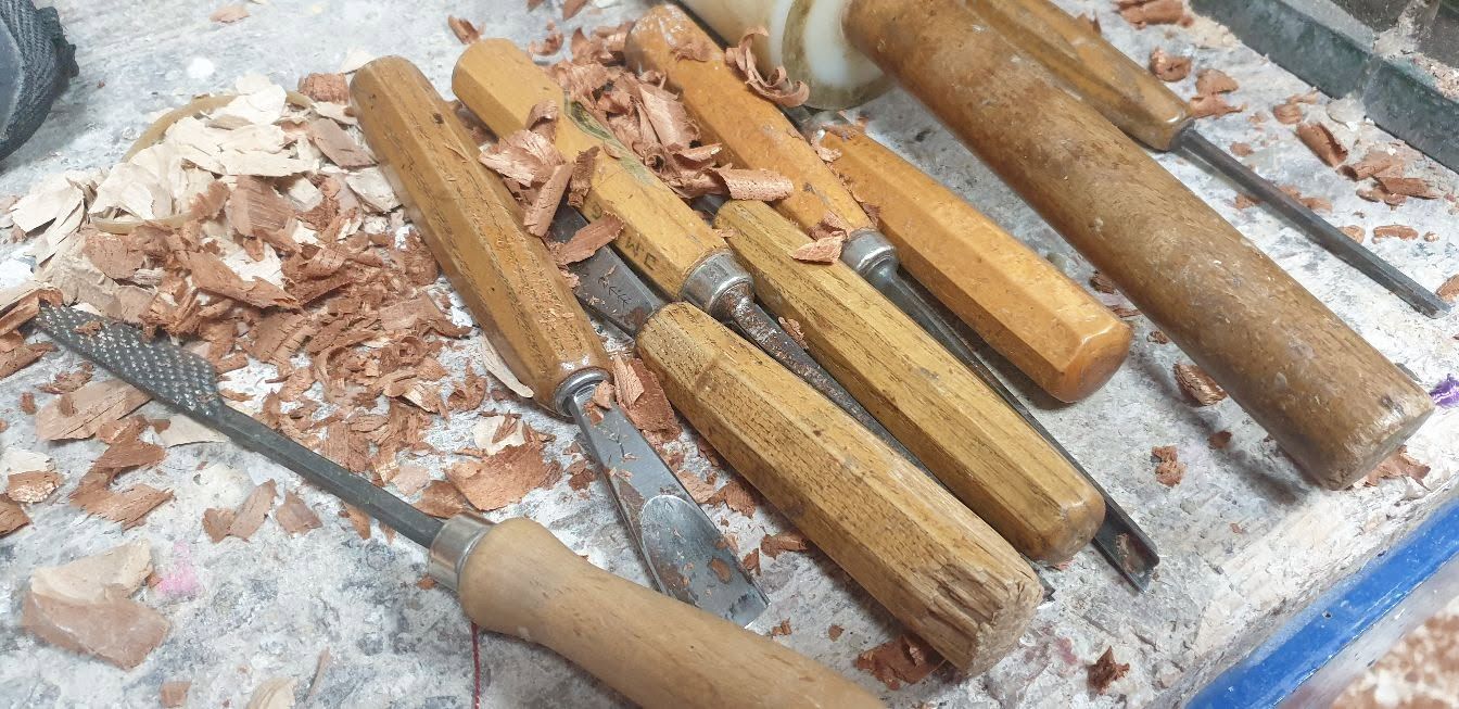 Varias herramientas y palos con mango de madera yacían en un suelo polvoriento entre escombros, algunos rotos o desgastados.