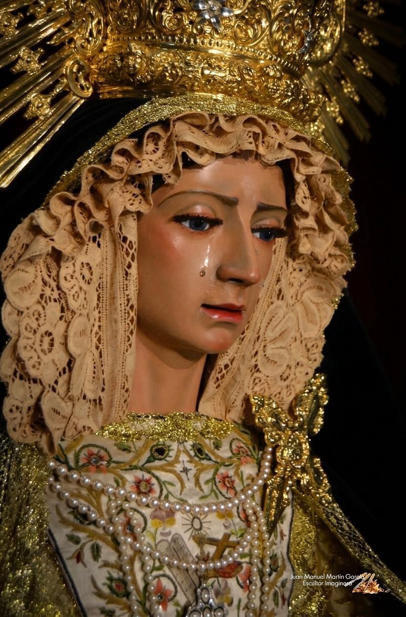 Estatua religiosa decorada con corona de oro, velo de encaje y vestimenta bordada, mostrada en primer plano.