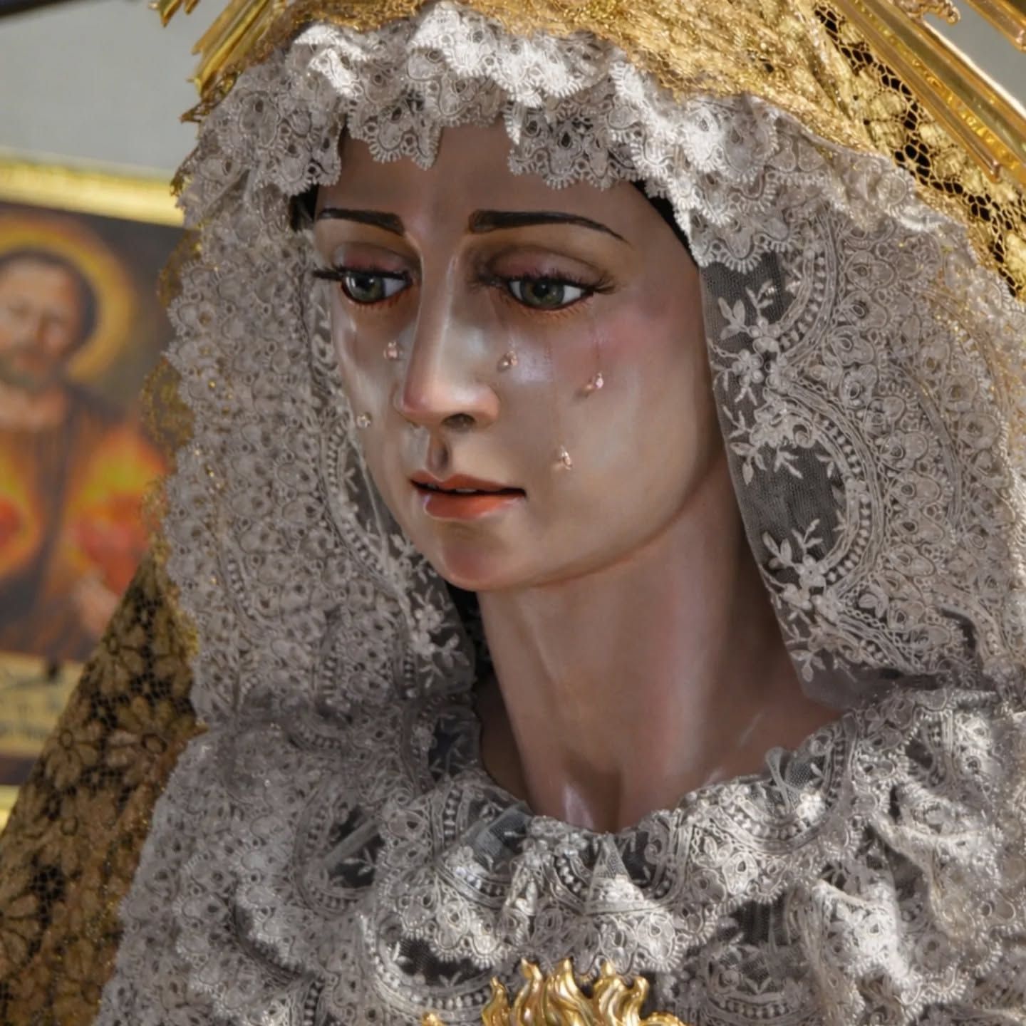 Una estatua velada de la Virgen María con marcas de lágrimas, en encaje blanco y ribete dorado.