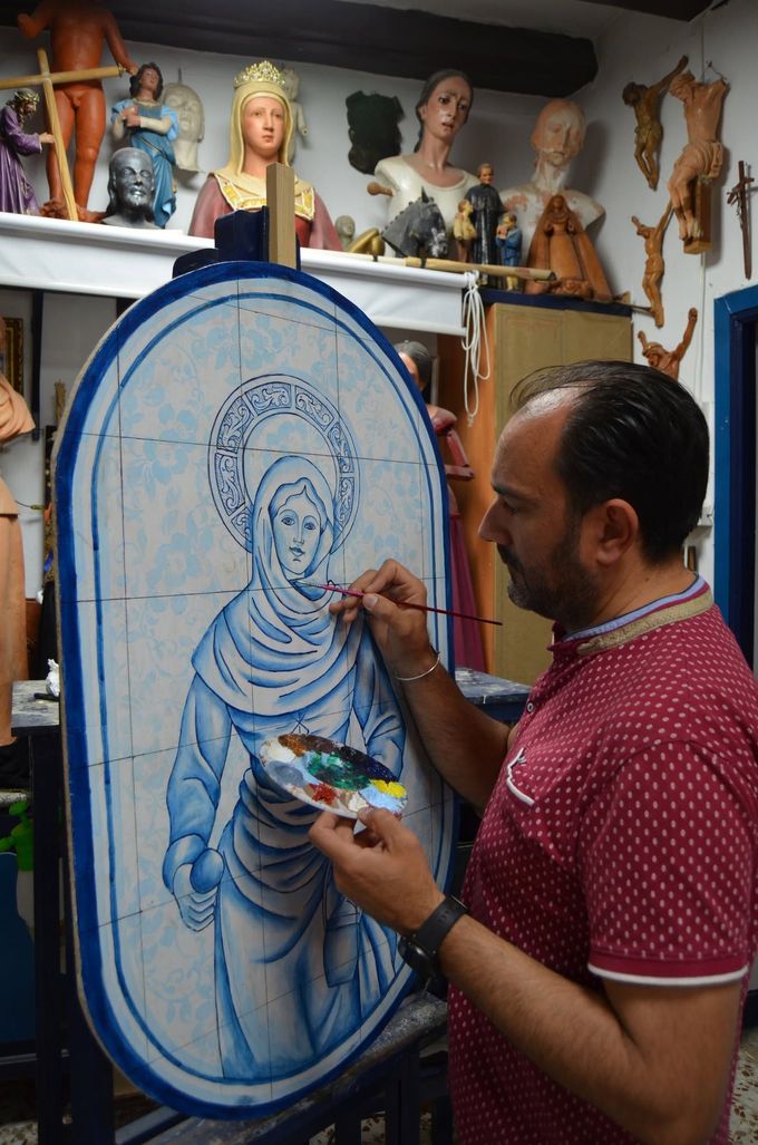 Un artista pinta un retrato azul sobre un gran lienzo ovalado en un estudio con esculturas y máscaras.