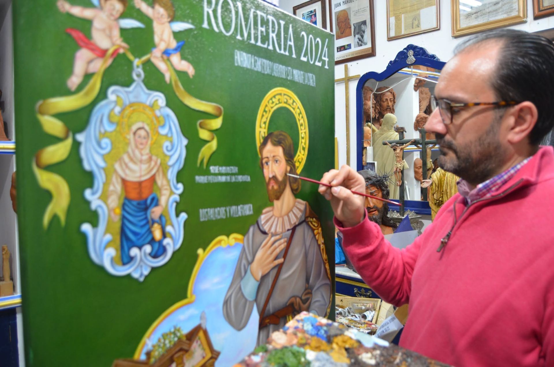 Artista pintando un colorido mural religioso con un santo en una pared verde.