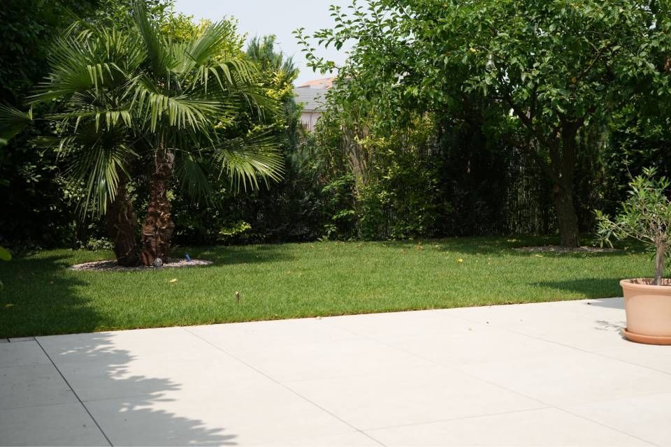 Terrasse mit hellen Fliesen, grünem Rasen und dichten tropischen Bäumen und Sträuchern im Hintergrund