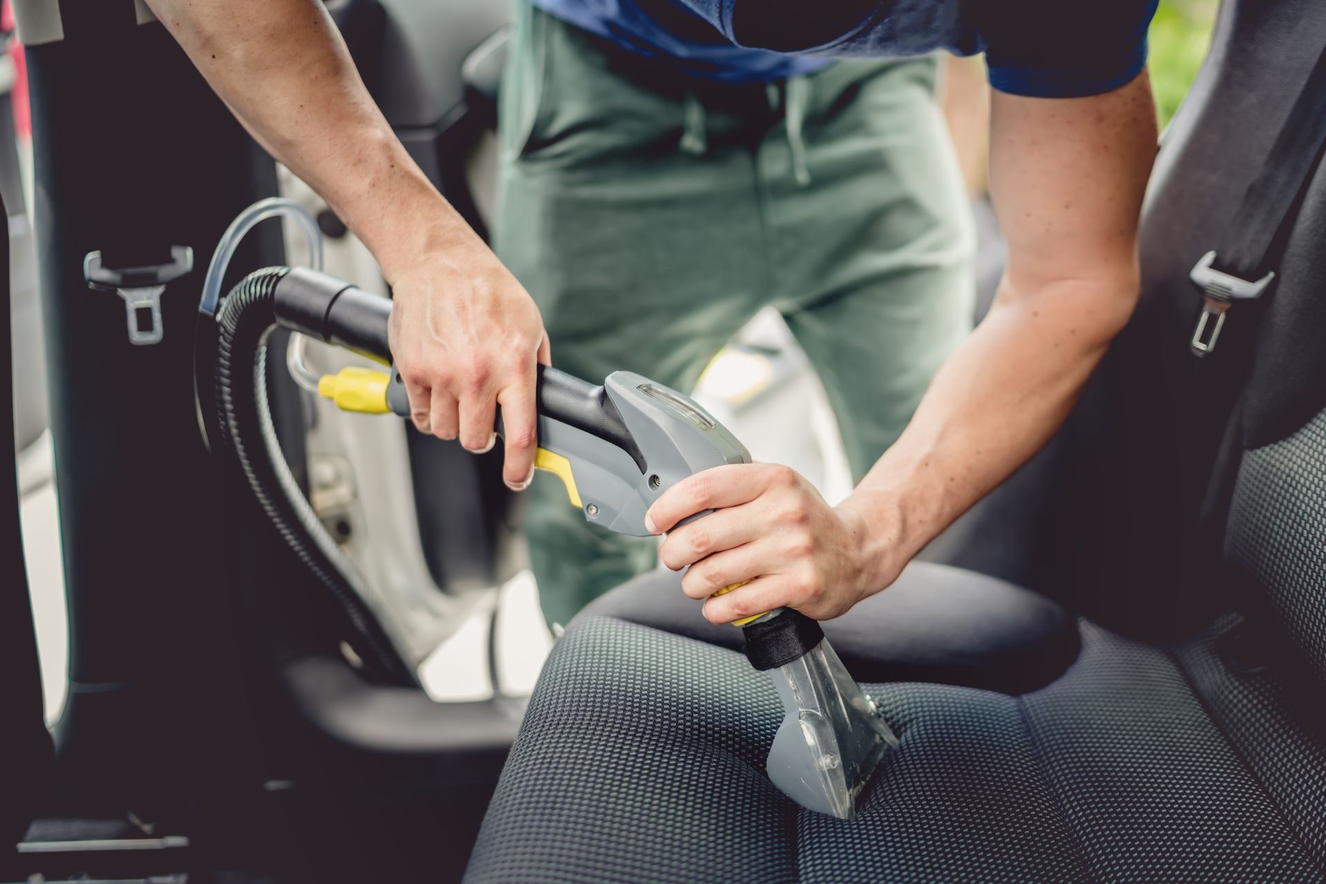 Une personne passe l'aspirateur sur les sièges de voiture avec un aspirateur portatif à l'intérieur d'un véhicule.