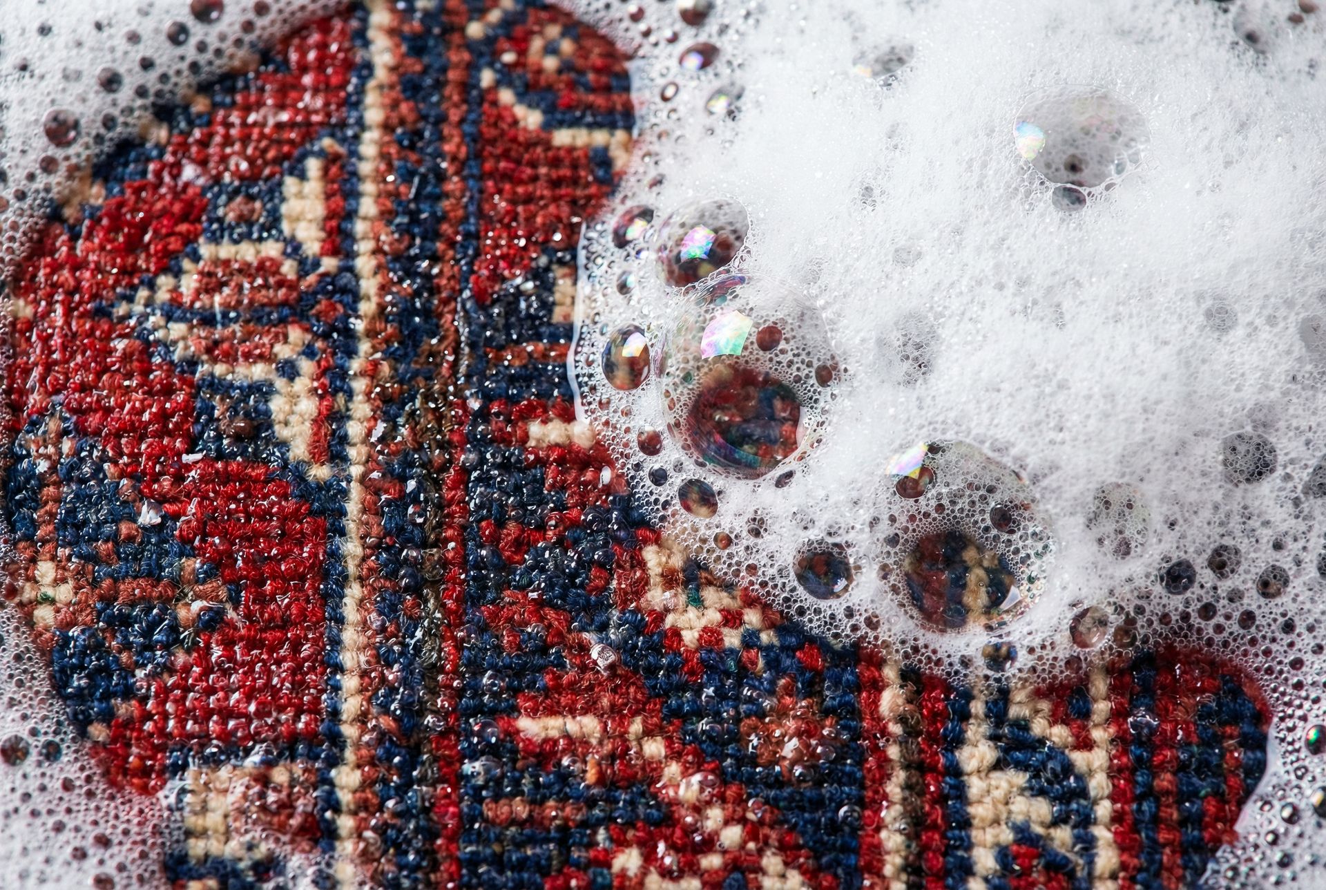 Bulles de savon mousseuses sur une surface de tissu à motifs rouges, bleus et beiges.