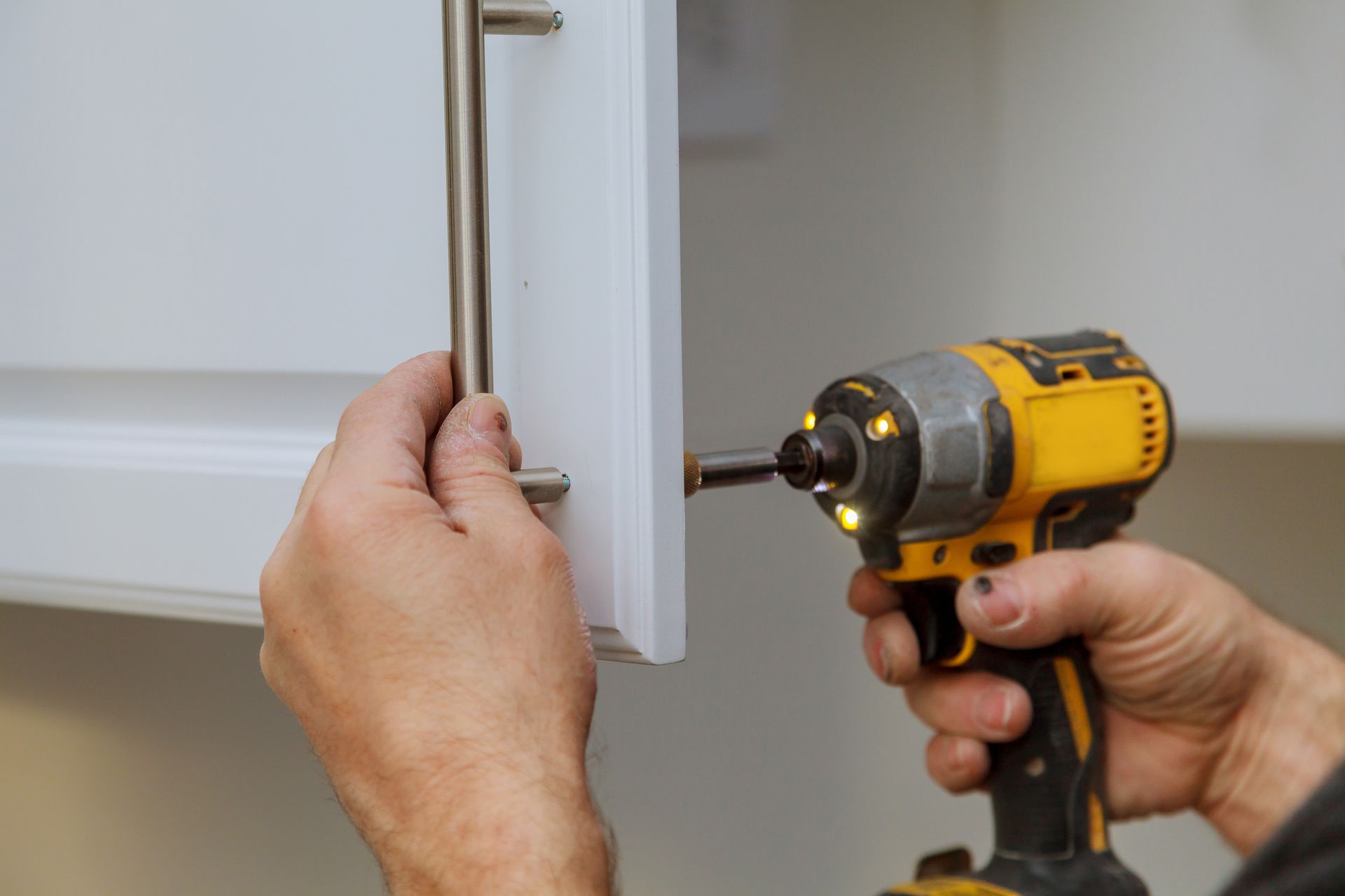 Des mains utilisent une perceuse pour installer une poignée de porte de placard blanche.