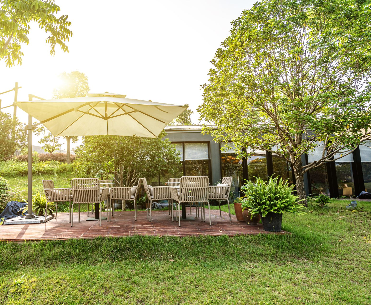 Terrasse extérieure ensoleillée avec tables, chaises et grands parasols, à côté d'un bâtiment et d'une pelouse verdoyante.