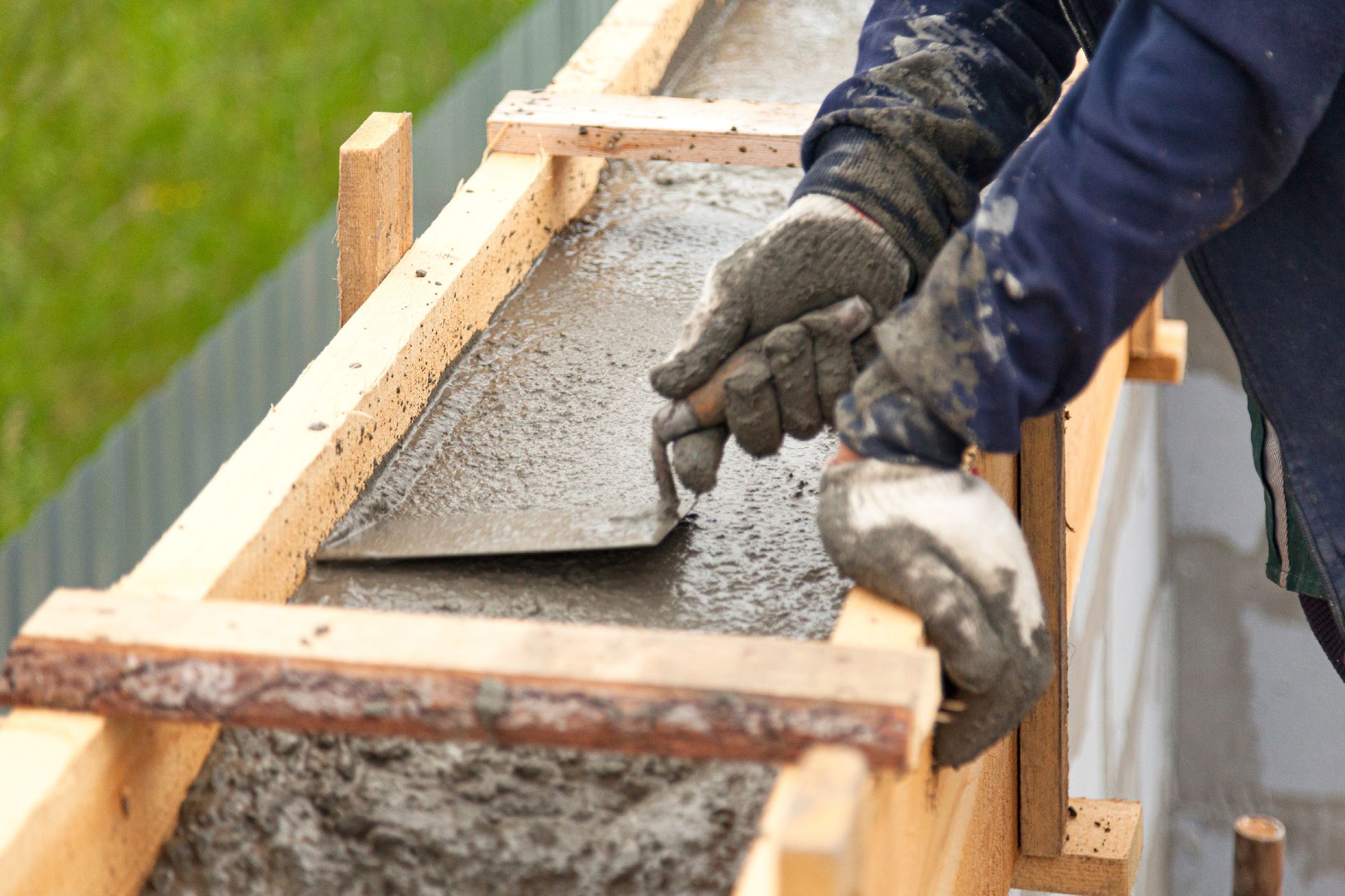 Des mains lissent du béton frais dans un coffrage en bois à l'extérieur.