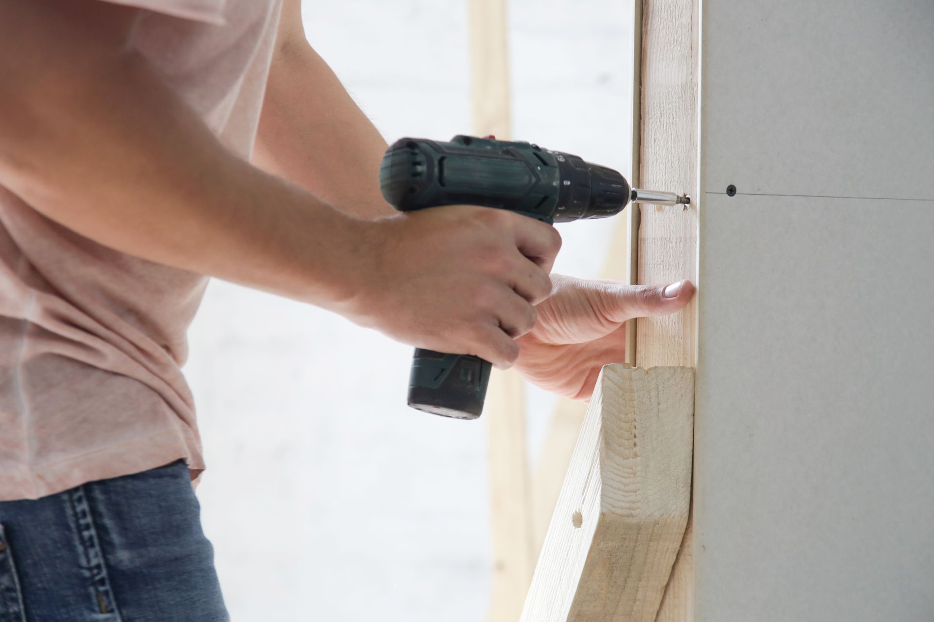 Une personne utilise une perceuse sans fil pour visser une planche dans un mur.