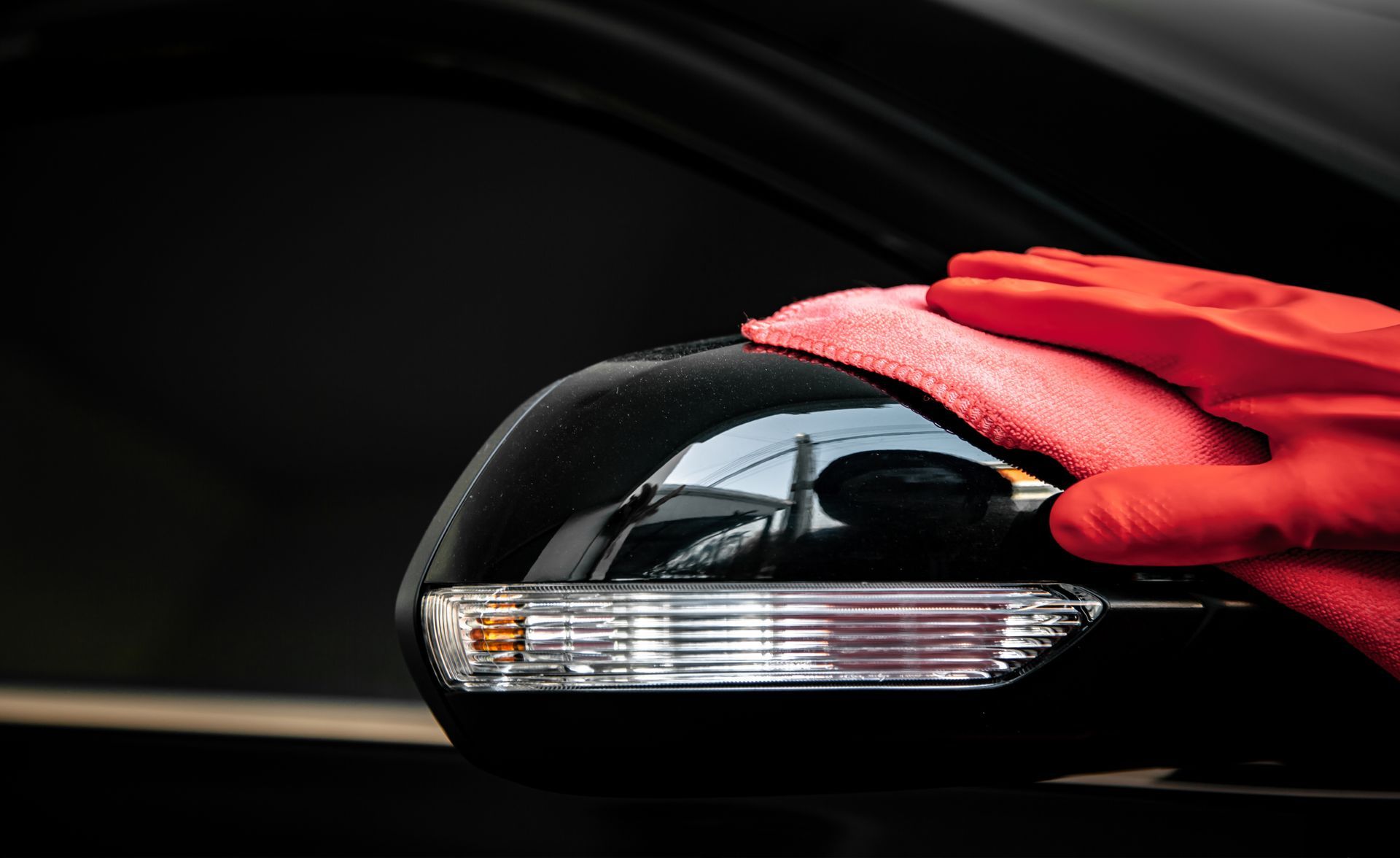 Main gantée de rouge posée sur une souris d'ordinateur noire sur fond sombre.
