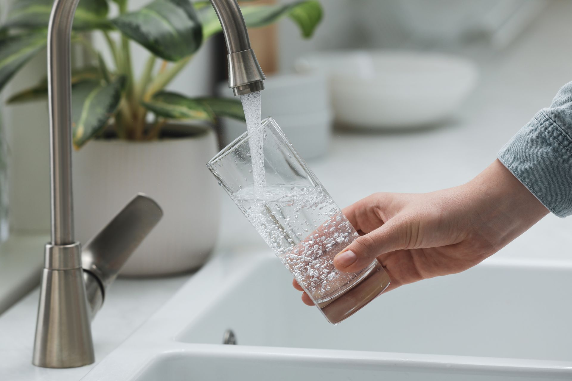 Se laver les mains sous le robinet de la cuisine, l'eau s'écoulant dans un verre transparent.
