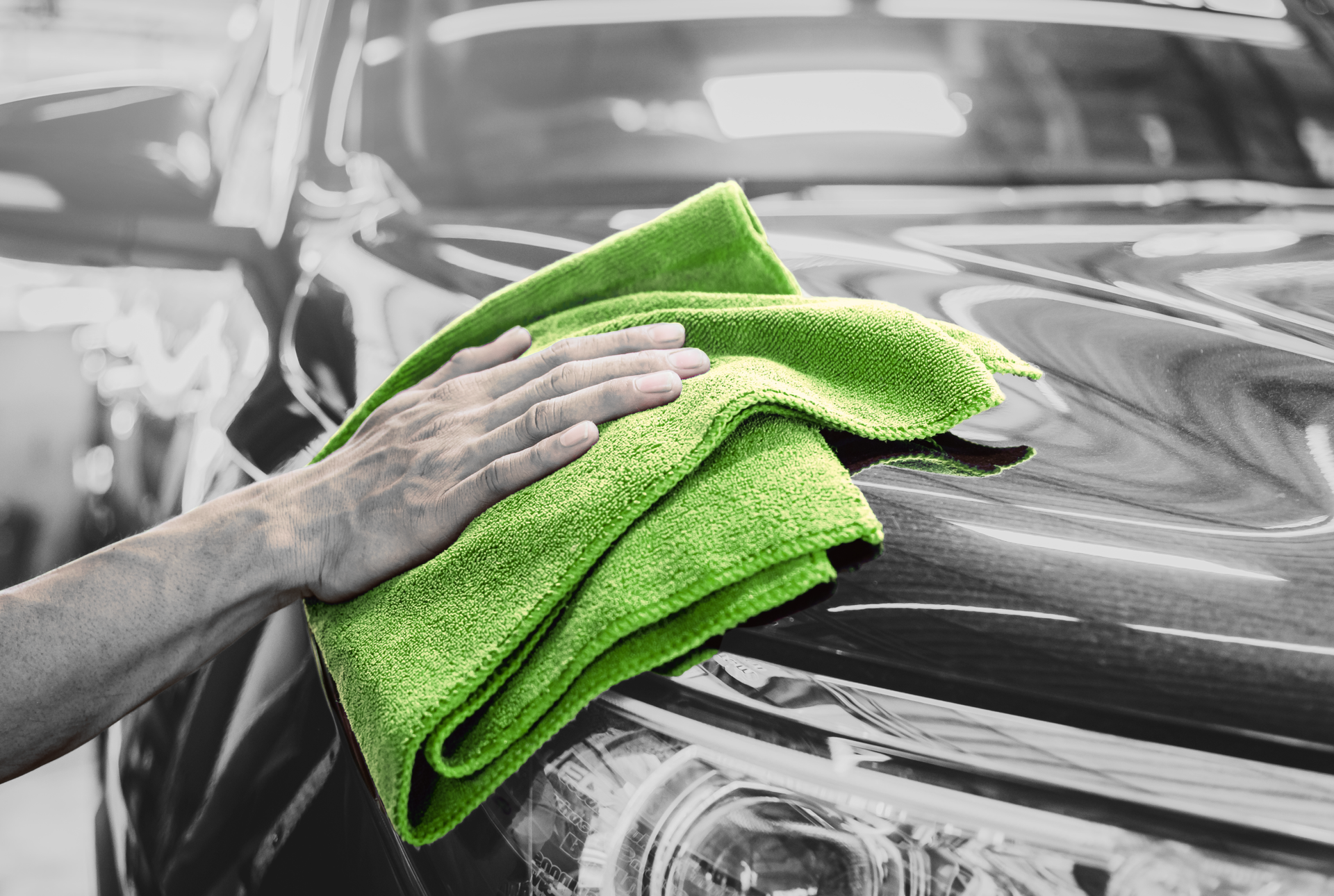Essuyage manuel de la surface d'une voiture noire avec un chiffon en microfibre vert vif dans un garage.