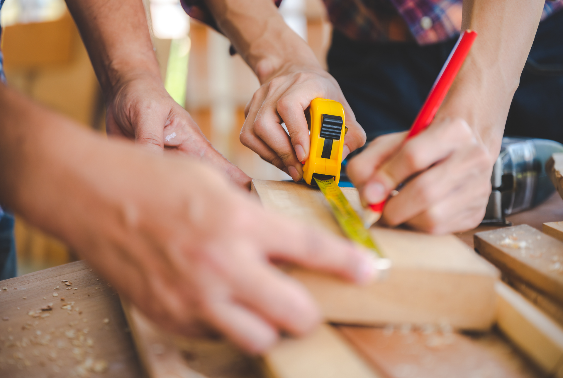 Des mains utilisent un mètre ruban et un crayon pour mesurer une planche sur un établi.