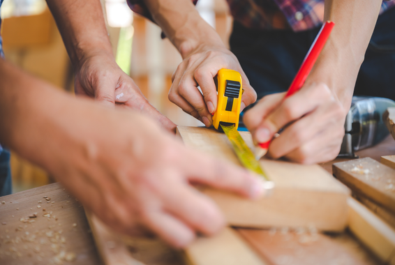 Des mains utilisent des outils pour mesurer et couper du bois dans un atelier.