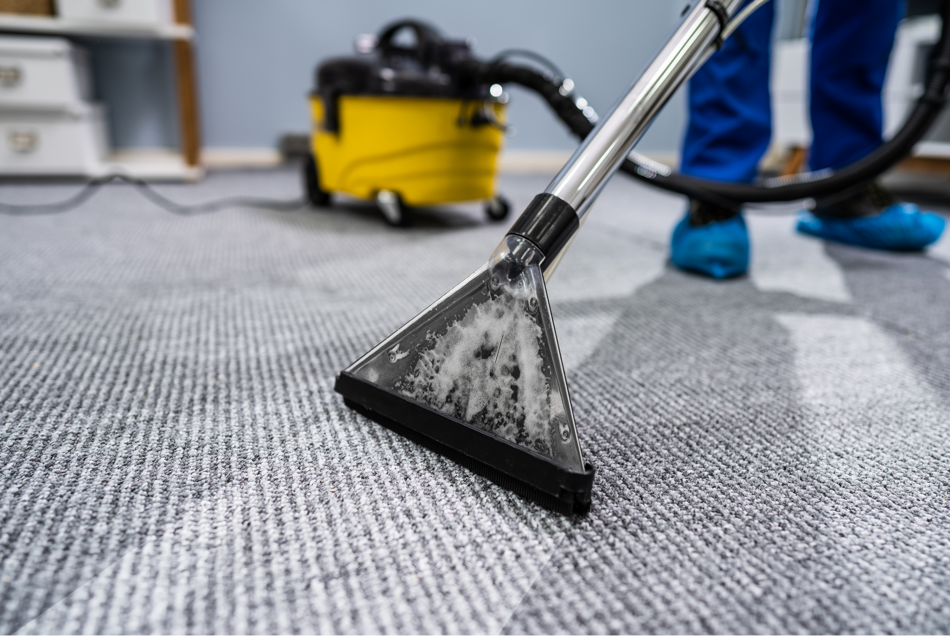 Aspirateur sur moquette grise avec une machine jaune en arrière-plan.