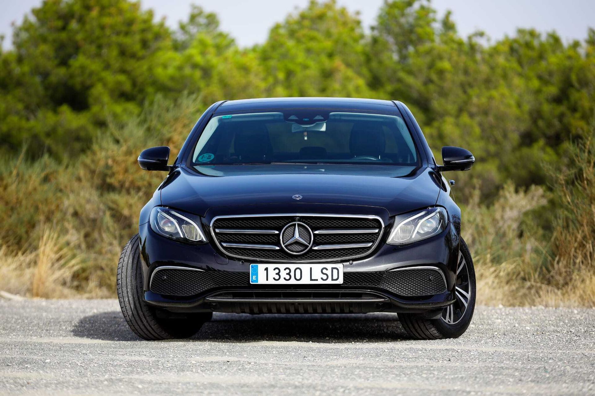 Un Mercedes Benz negro está estacionado en un camino de tierra.