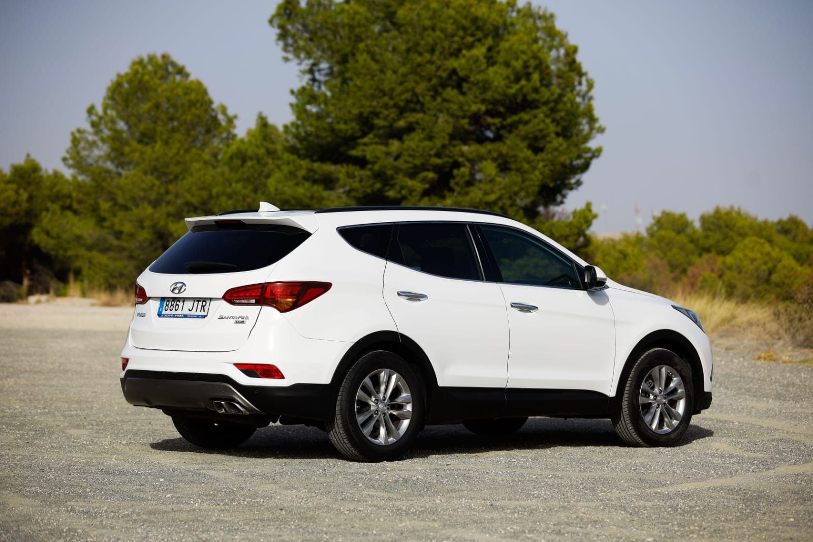 Una camioneta blanca está estacionada en un lote de grava con árboles al fondo.
