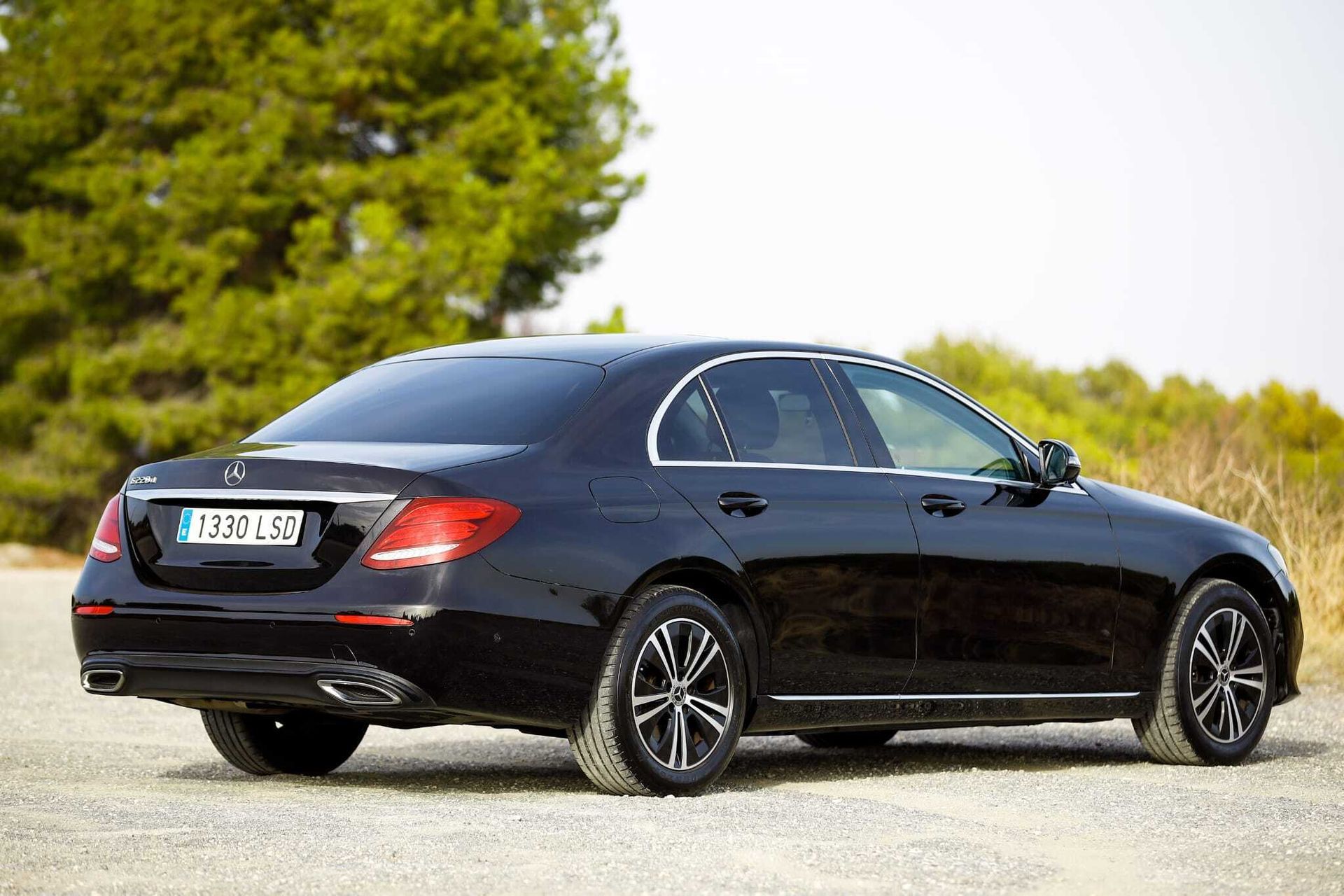 Un Mercedes Benz Clase E negro está estacionado en un camino de grava.
