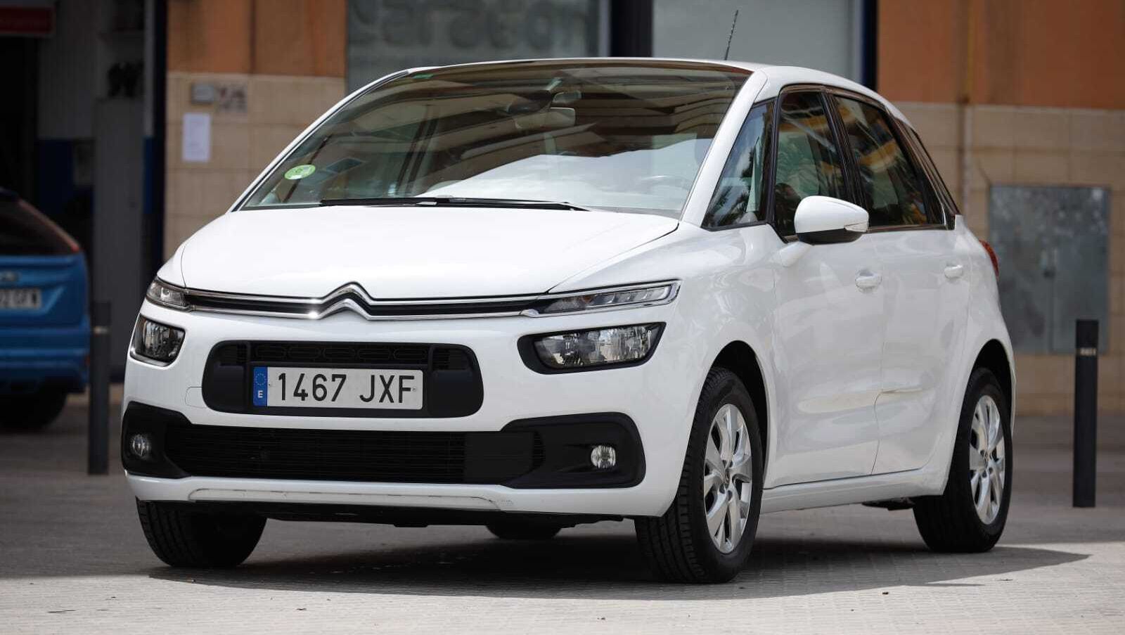 Un Citroën C4 Picasso blanco está estacionado delante de un edificio.