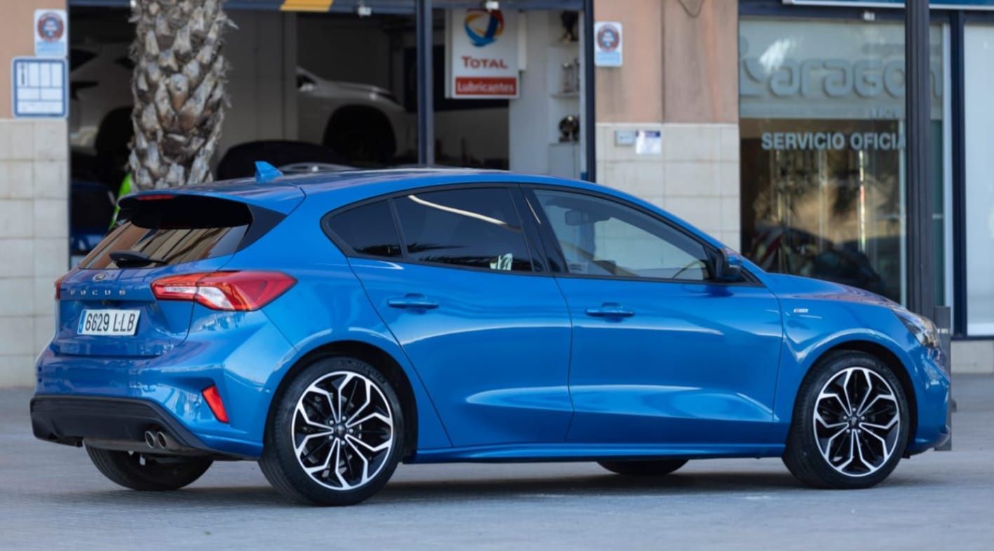 Un Ford Focus hatchback azul está estacionado frente a un edificio.