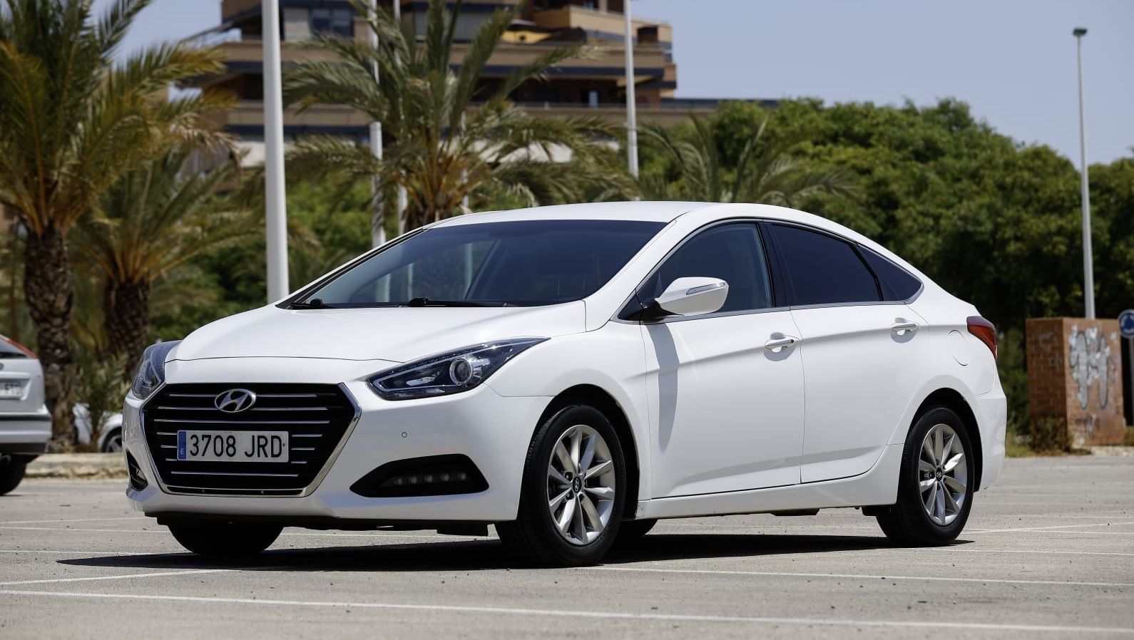 Un Hyundai blanco está estacionado en un estacionamiento con palmeras al fondo.