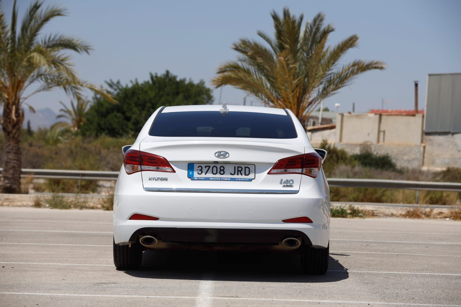 Un coche blanco está aparcado en un estacionamiento con palmeras al fondo.