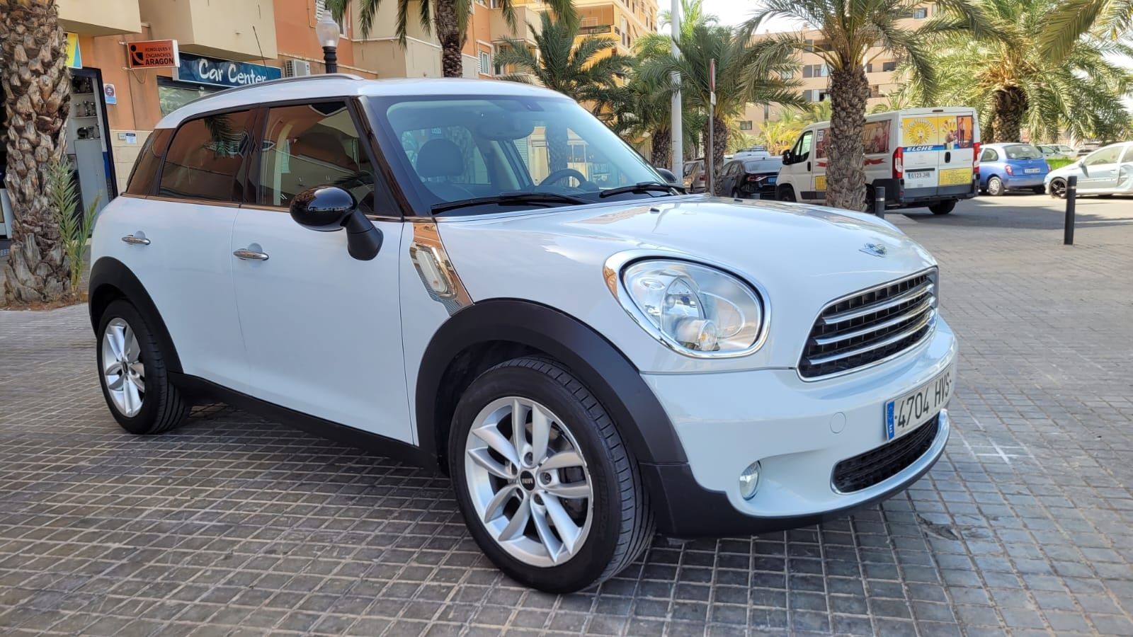 Un Mini Cooper Countryman blanco está estacionado en una acera de ladrillos.