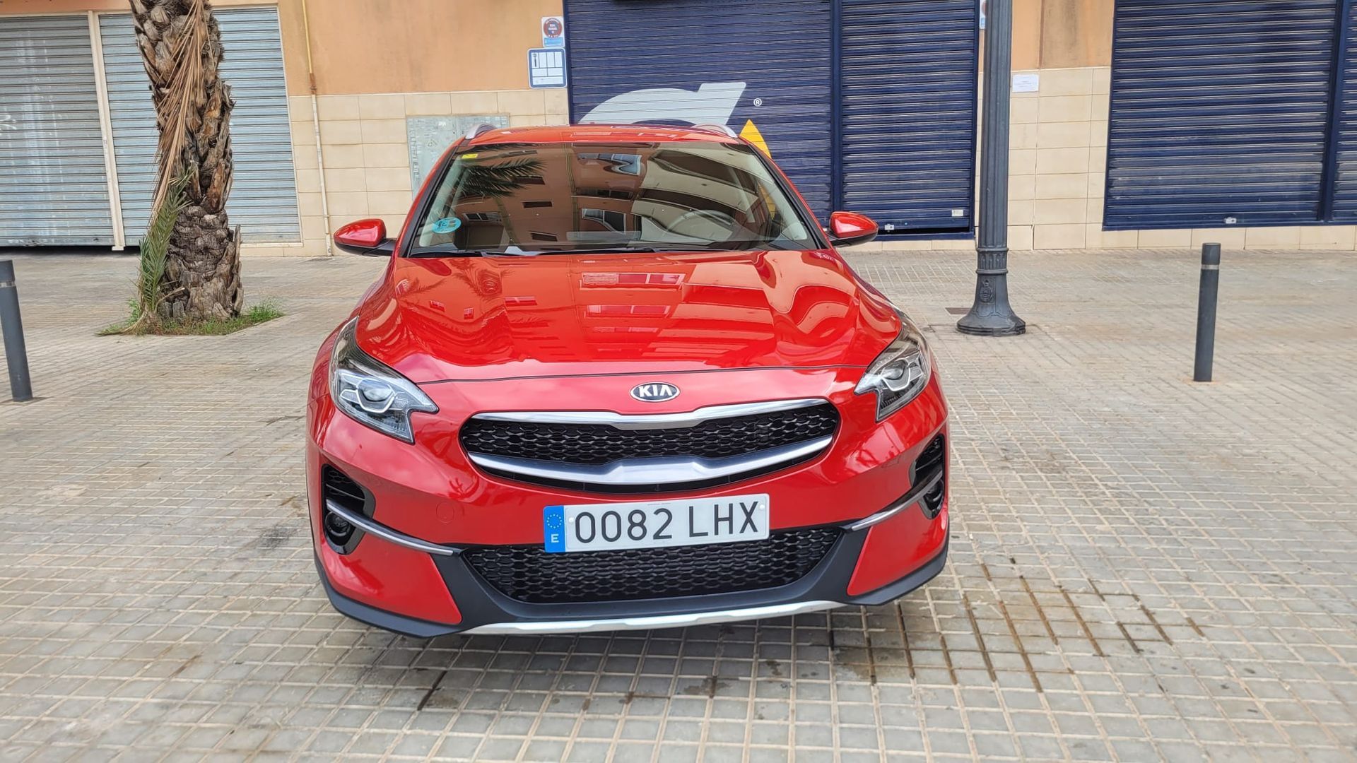 Un coche rojo está estacionado en una acera de ladrillos frente a un edificio.