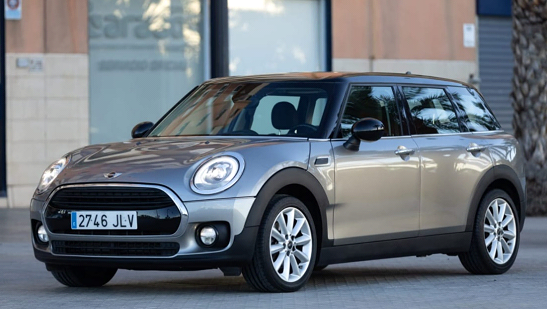 Un Mini Cooper Clubman plateado está estacionado frente a un edificio.