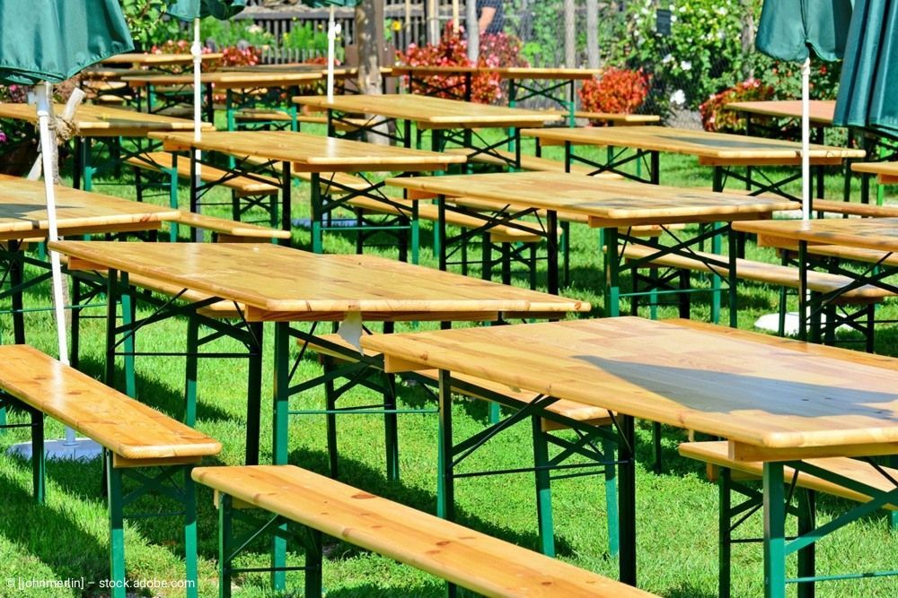 Hölzerne Picknicktische und Bänke auf grünem Rasen, im Freien für ein Treffen aufgestellt.